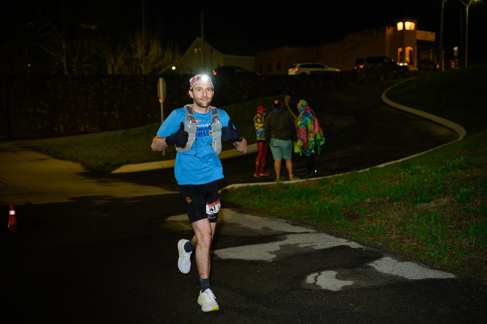 Egan running an ultra at night, headlamp on, thumbs up